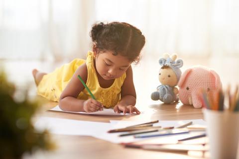 Young child lying on the floor and coloring pages